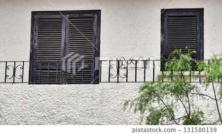 A charming white building with black shutters and a balcony tree A charming white building with black shutters and a balcony tree 131580139