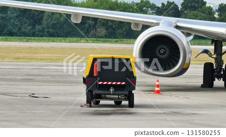 An Aircraft Ground Support Vehicle Positioned Close to a Jet Engine at the Airport tarmac An Aircraft Ground Support Vehicle Positioned Close to a Jet Engine at the Airport tarmac 131580255