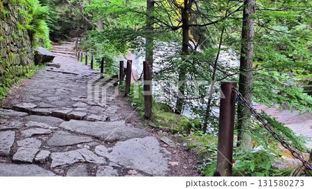 A scenic and picturesque stone pathway meanders gracefully alongside a serene riverbank 131580273