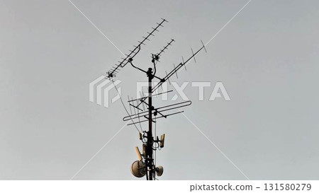 A diverse antenna array mounted on a communication tower stands prominently against a gray sky 131580279