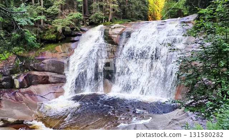 A serene waterfall cascades gracefully through a lush green forest rich in nature 131580282