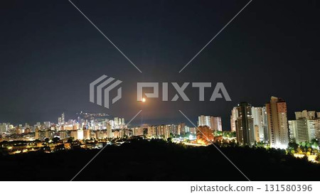 A Stunning Night Cityscape with a Full Moon and Beautiful Urban Lights shining brightly 131580396