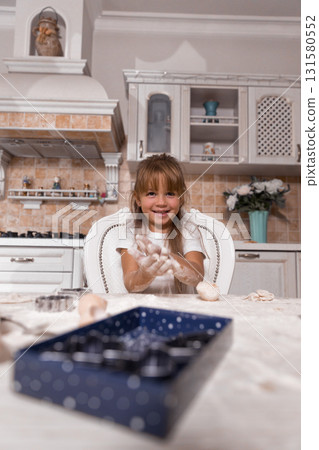 young girl in a sunny kitchen has fun making a cake. She smiles and plays with flour while surrounded by baking tools showing her excitement and creativity during this enjoyable afternoon. young girl in a sunny kitchen has fun making a cake. She smiles and plays with flour while surrounded by baking tools showing her excitement and creativity during this enjoyable afternoon. 131580552