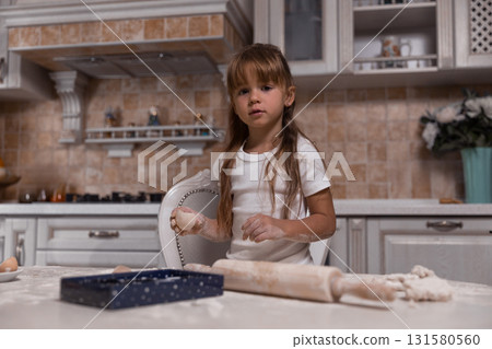 young girl is happily making a cake in a well designed kitchen. Flour covers the table as she rolls dough showcasing her enthusiasm for baking and creating delicious treats. young girl is happily making a cake in a well designed kitchen. Flour covers the table as she rolls dough showcasing her enthusiasm for baking and creating delicious treats. 131580560