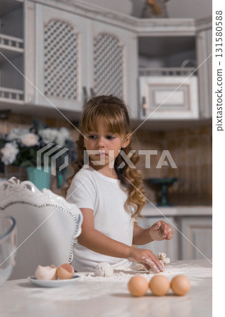 young girl with curly hair is focused on making a cake. She is preparing the ingredients on the countertop showcasing her baking skills. 131580588