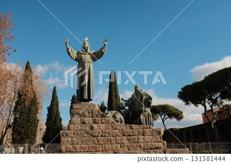 Statue of Saint Francis of Assisi with open arms in garden near Basilica of Saint Mary Major Rome Italy blue sky stone sculpture religious monument landmark no people. High quality photo 131581444