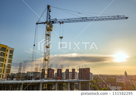 Apartment or office tall building under construction. Brick walls, glass windows, scaffolding and concrete support pillars. Tower crane on bright blue sky copy space background. 131582295