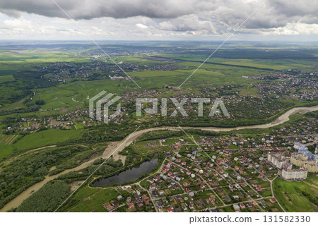 Aerial view of town or village with rows of buildings and curvy streets between green fields in summer. Countryside landscape from above. 131582330