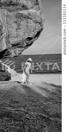 Woman in Hat Walks on Rocky Beach 131583114