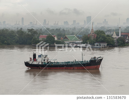 A large cargo ship on the Chao Phraya River with a city skyline and Wat Bangkrachaonok in the background. The sky after the rain is always beautiful, 131583670