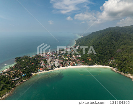 Lush green hills meeting the turquoise sea along a tropical coastline under a bright blue sky. Ko Pha Ngan, Thailand. Lush green hills meeting the turquoise sea along a tropical coastline under a bright blue sky. Ko Pha Ngan, Thailand. 131584365
