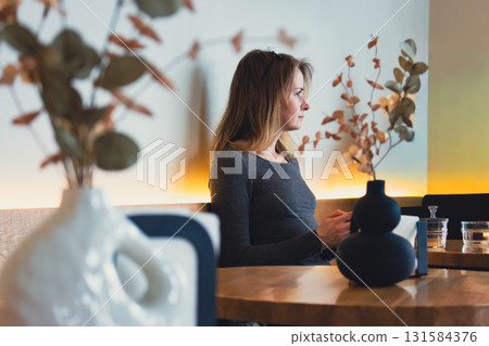 Woman in cafe texting message in phone. Autumn cozy cafe. Girl sitting on couch in restaurant with nice decor. Beautiful girl in elegant cafe interior. Cozy lifestyle. Modern lifestyle. Woman in cafe texting message in phone. Autumn cozy cafe. Girl sitting on couch in restaurant with nice decor. Beautiful girl in elegant cafe interior. Cozy lifestyle. Modern lifestyle. 131584376