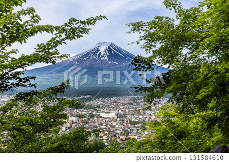 Scenic view of Mount Fuji overlooking Fujiyoshida City in springtime framed with lush green foliage in foreground Scenic view of Mount Fuji overlooking Fujiyoshida City in springtime framed with lush green foliage in foreground 131584610