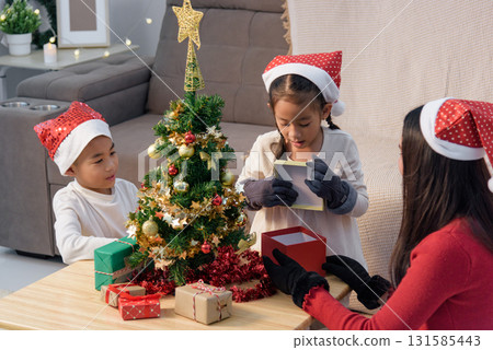 Christmas family home, parent child decorate small tree, then enjoy holiday gift box unwrapping, boy watches girl with festive Christmas cheer. Christmas family home, parent child decorate small tree, then enjoy holiday gift box unwrapping, boy watches girl with festive Christmas cheer. 131585443