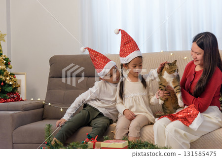 Christmas family home holiday, parent child decorating home with gifts, joyfully sharing time, children wear Santa hats near bright Christmas tree, gentle cat adds festive cheer. 131585475