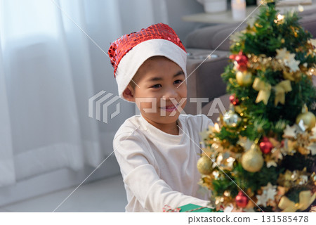 Christmas holiday joy brightens family home child wearing Santa hat holds gift box near sparkling festive Christmas tree decorations young boy smiles enjoying special day. 131585478