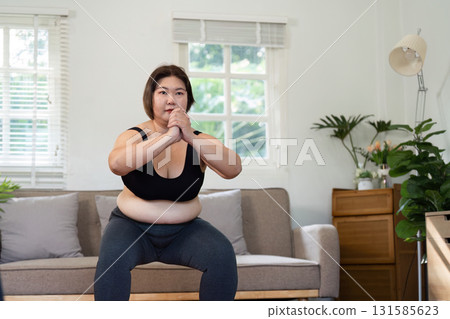 Strength Training and Empowerment. A woman confidently performing a squat exercise at home, building her strength. 131585623