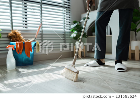 Cleaning and Home Care. A dedicated cleaner using a broom to tidy up the floor in a modern living space, focused on maintaining cleanliness. 131585624