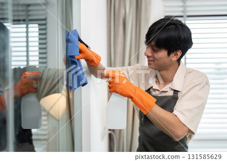 Window Cleaning and Professional Services. A diligent cleaner uses a spray bottle and cloth to clean glass surfaces, smiling while working. Window Cleaning and Professional Services. A diligent cleaner uses a spray bottle and cloth to clean glass surfaces, smiling while working. 131585629