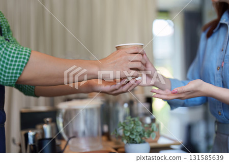 Cafe Experience and Barista Interaction. A customer receiving a takeout coffee cup from a barista emphasizing customer service. 131585639