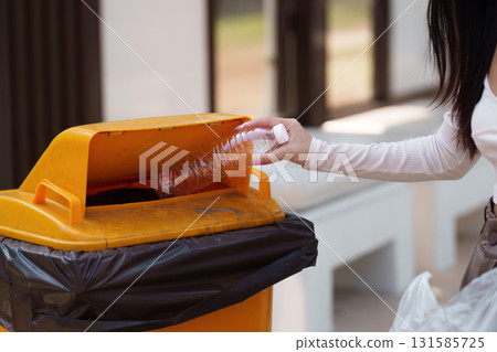 Individual recycling plastic bottles in a yellow bin, promoting sustainability and waste management. 131585725