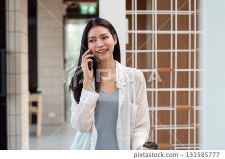 Sustainable Communication and Urban Lifestyle. A young woman smiles on her phone, showcasing the modern blend of technology and social interaction. 131585777