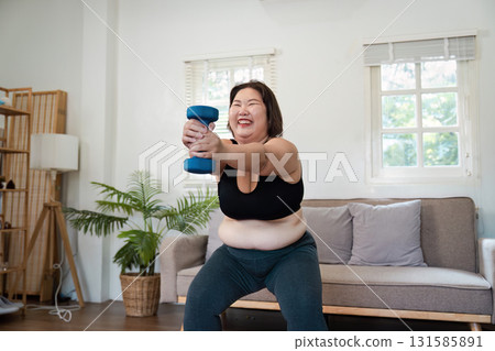 Wellness and Fitness. Plus-size woman exercising with dumbbells in a bright home setting. 131585891