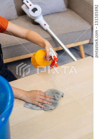 Close-up of a woman spraying cleaner on a table while cleaning at home. 131585892