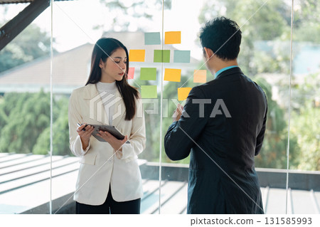 Business team brainstorming with sticky notes in a modern office, discussing project strategies Business team brainstorming with sticky notes in a modern office, discussing project strategies 131585993