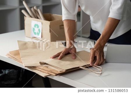 Individual organizing paper bags for recycling, promoting sustainable practices in daily life. 131586053