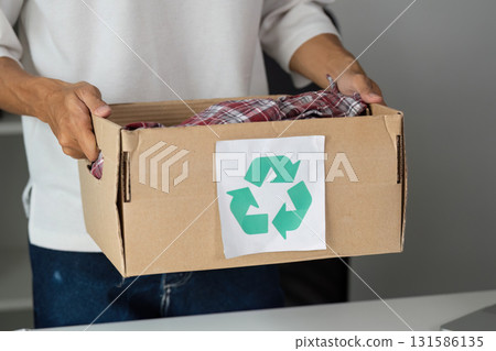 Person holding a donation box filled with clothes, emphasizing recycling and sustainable practices. Person holding a donation box filled with clothes, emphasizing recycling and sustainable practices. 131586135