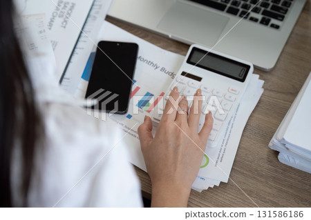 Detail-oriented financial analyst calculating budget using a calculator and reviewing financial reports. Detail-oriented financial analyst calculating budget using a calculator and reviewing financial reports. 131586186