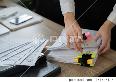 Professional accountant organizing financial documents on a desk with colorful clips and reports. Professional accountant organizing financial documents on a desk with colorful clips and reports. 131586187