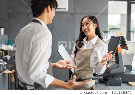 Cafe staff happily discussing daily operations with a clipboard and tablet 131586345