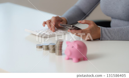 Financial Empowerment. Woman managing savings with smartphone and piggy bank. 131586405