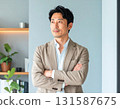 A middle-aged Japanese businessman in his 40s, wearing a beige jacket, standing in his office with his arms crossed and a confident look on his face 131587675