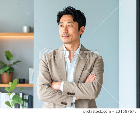 A middle-aged Japanese businessman in his 40s, wearing a beige jacket, standing in his office with his arms crossed and a confident look on his face 131587675