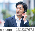 A Japanese middle-aged businessman in his 40s talking outdoors with a smartphone to his ear and a smile 131587678
