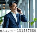 A middle-aged Japanese businessman in his 50s holds a smartphone to his ear in the office and talks on the phone with a serious expression 131587680