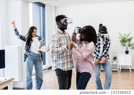 Diverse group of young adults enjoying interactive VR technology, experiencing fun and teamwork. Office-like environment expresses a combination of relaxation and technology. Diverse group of young adults enjoying interactive VR technology, experiencing fun and teamwork. Office-like environment expresses a combination of relaxation and technology. 131590932