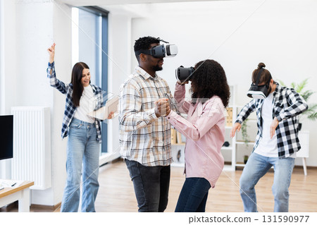 Young adults wearing virtual reality headsets interacting playfully in a modern room creating joyful and innovative moments. Engaged in technology and entertainment, embracing contemporary leisure. Young adults wearing virtual reality headsets interacting playfully in a modern room creating joyful and innovative moments. Engaged in technology and entertainment, embracing contemporary leisure. 131590977