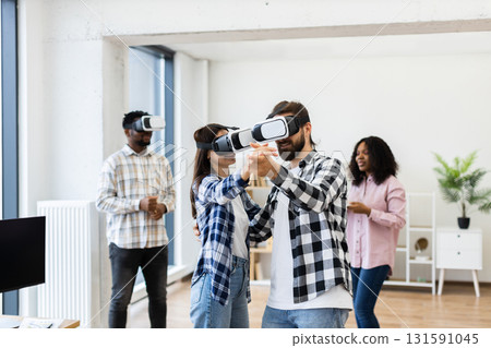 Young adults wearing VR headsets engaged in interactive activity, simulating dance and entertainment. Group consisting of men and women having fun with innovative wearable technology. Young adults wearing VR headsets engaged in interactive activity, simulating dance and entertainment. Group consisting of men and women having fun with innovative wearable technology. 131591045