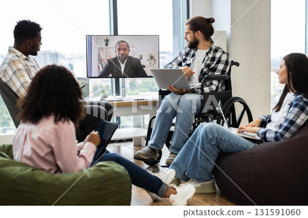 Group of young professionals collaborating in office during video call with male manager. Meeting showcases workspace diversity including individuals of different ethnicities and backgrounds. Group of young professionals collaborating in office during video call with male manager. Meeting showcases workspace diversity including individuals of different ethnicities and backgrounds. 131591060