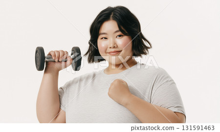 A woman holds a dumbbell and smiles cheerfully on a white background 131591463