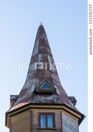 Close-up view of an old wooden tower with a steep, weathered conical roof and small triangular Close-up view of an old wooden tower with a steep, weathered conical roof and small triangular 131592727