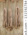 Bundles of various types of rope hang from the wall of a seaside warehouse. 131592784