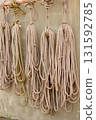 Bundles of various types of rope hang from the wall of a seaside warehouse. 131592785