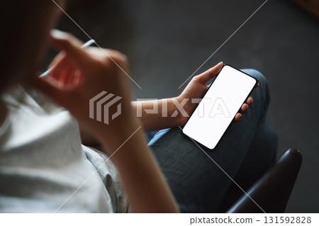 Young woman sitting in chair and holding smartphone with white screen 131592828