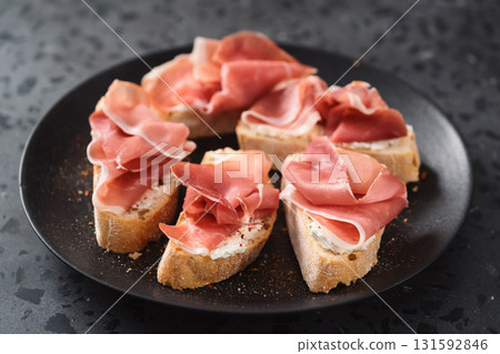 bruschetta with prosciutto and cream cheese on black plate on conctere background 131592846