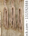 Bundles of various types of rope hang from the wall of a seaside warehouse. 131592888